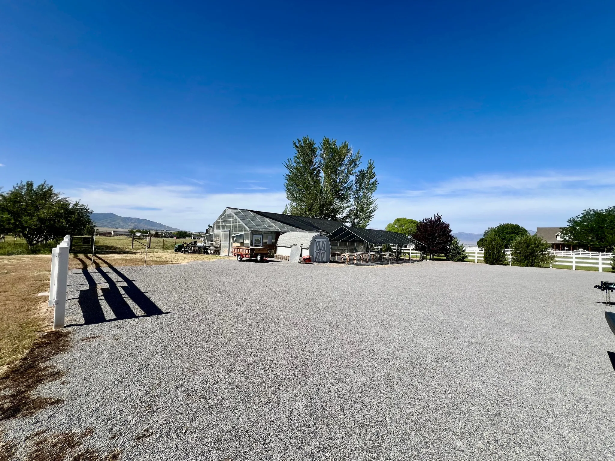 Expansive gravel lot featuring a large greenhouse structure with a clear roof and dark siding
