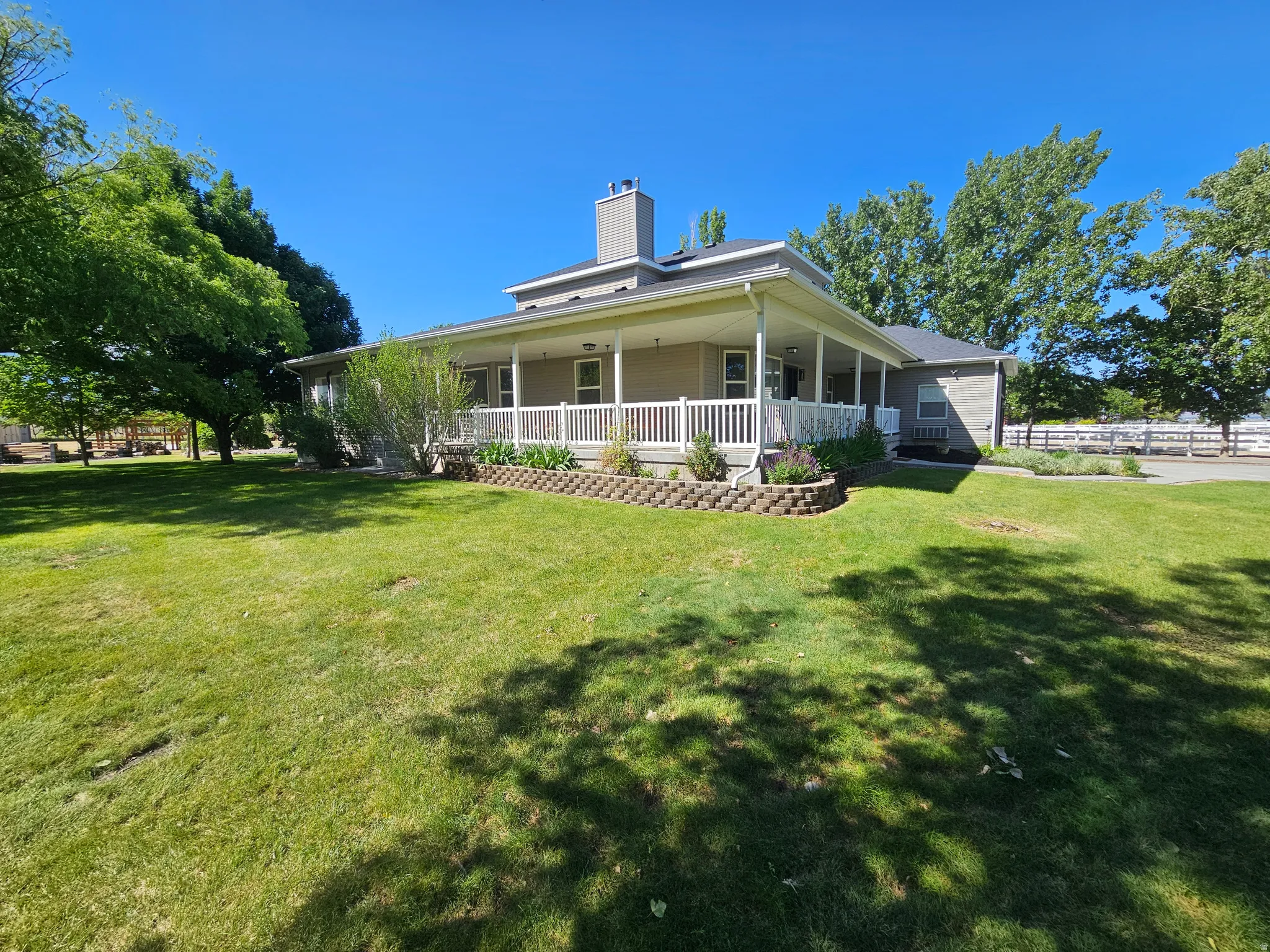 Expansive green lawn bordering a residence with a wraparound porch featuring white railings