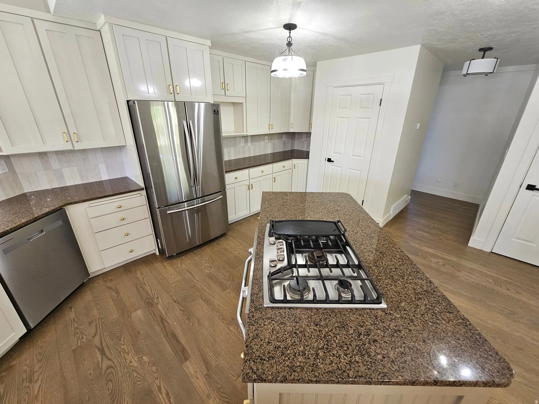 Kitchen featuring an island with an integrated gas cooktop, white cabinetry with gold-tone hardware, stainless steel appliances, speckled countertops, and wood-finish flooring
