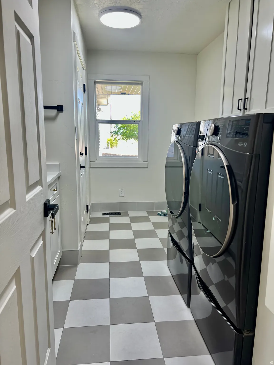 Laundry area featuring checkerboard flooring, white shaker cabinetry, a built-in countertop, a window with white trim, and a flush-mount ceiling light