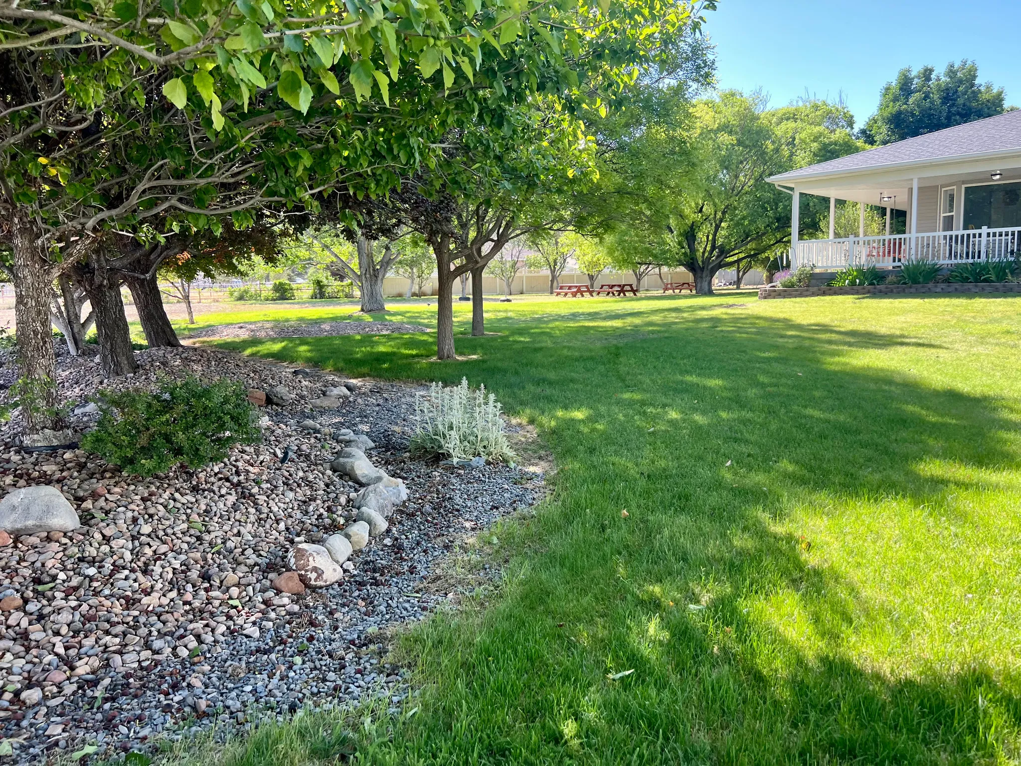 Spacious green lawn surrounded by mature trees, featuring a stone and gravel landscape bed, and a covered porch