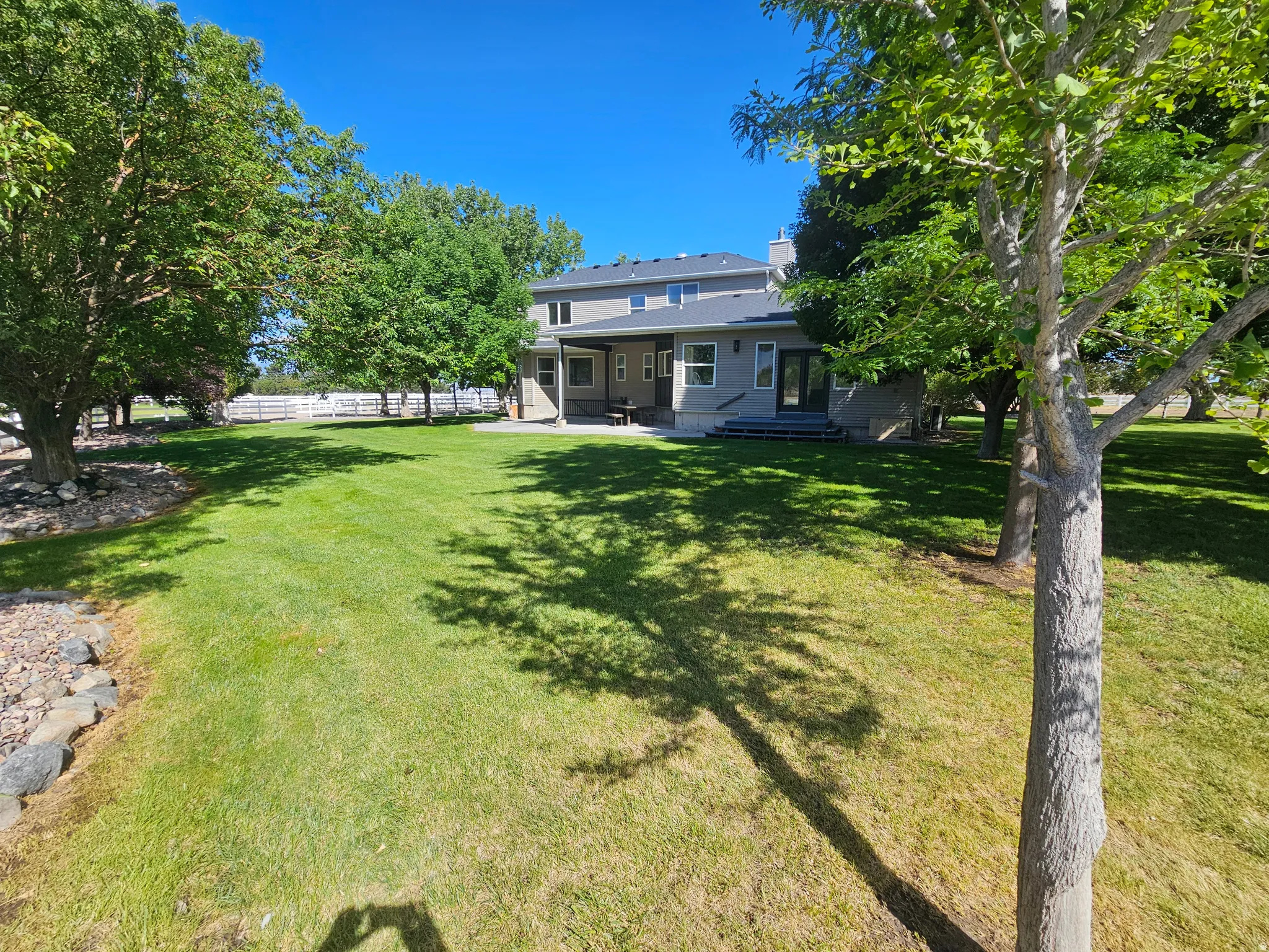 Expansive backyard featuring a manicured lawn, mature trees, and a white fence border
