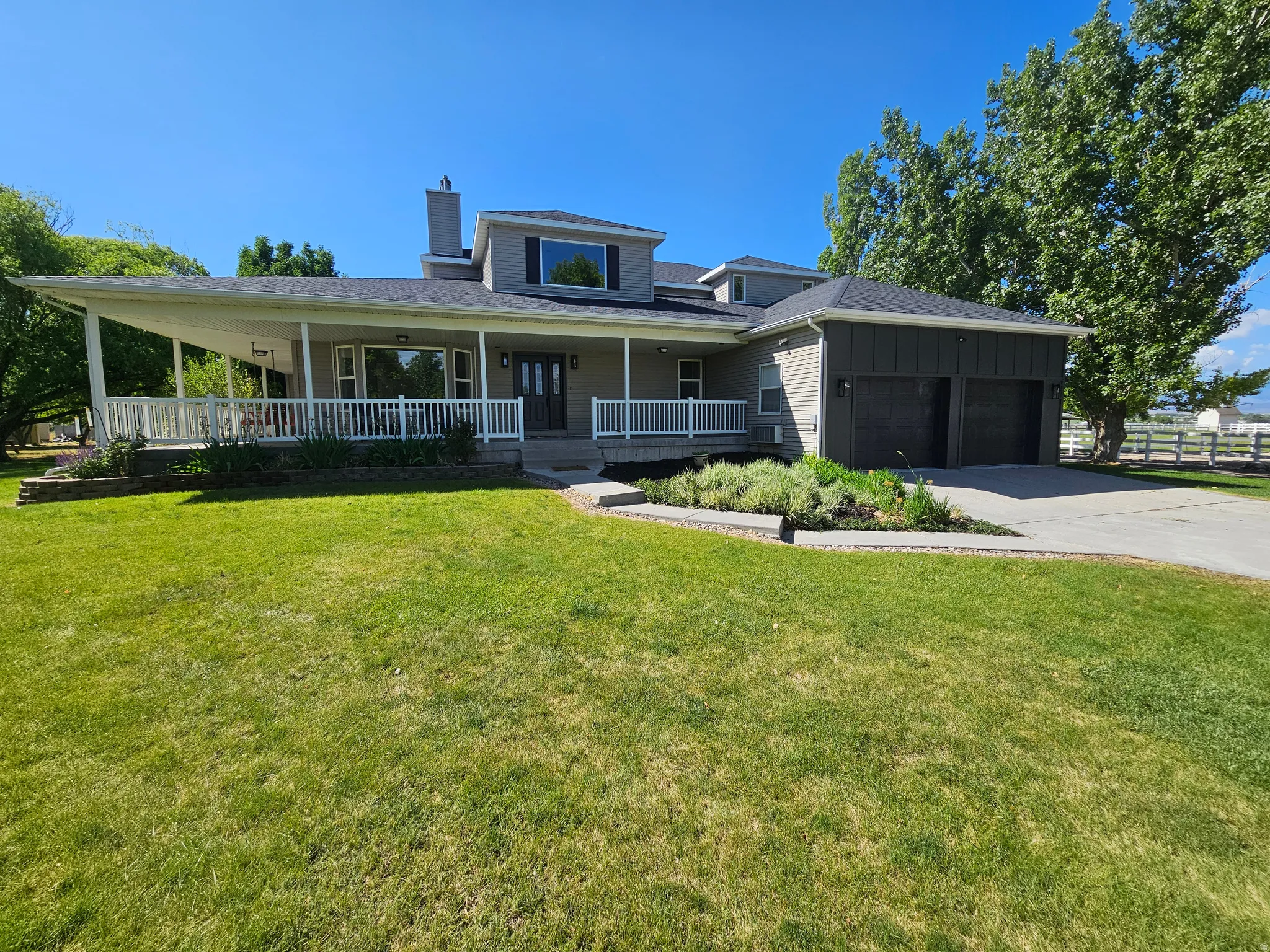 Contemporary two-story residence featuring a covered wrap-around porch with white railings, an attached two-car garage with dark paneled doors, and a paved driveway