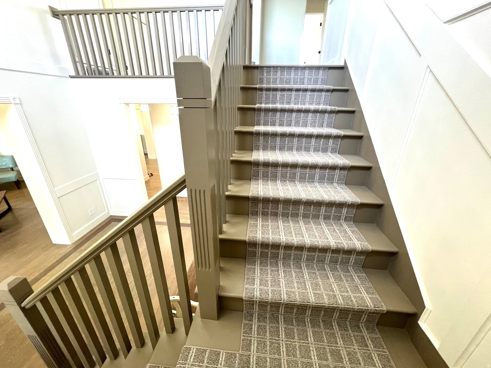 Staircase with patterned runner, painted balusters, and a paneled wall