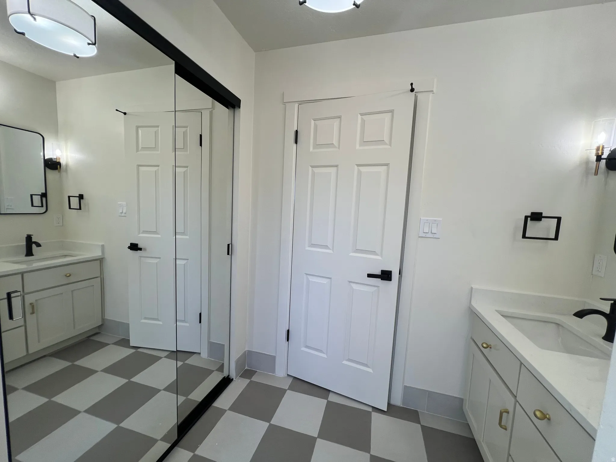 Bathroom featuring a checkered tile floor, dual vanity sinks with light countertops, and white cabinetry