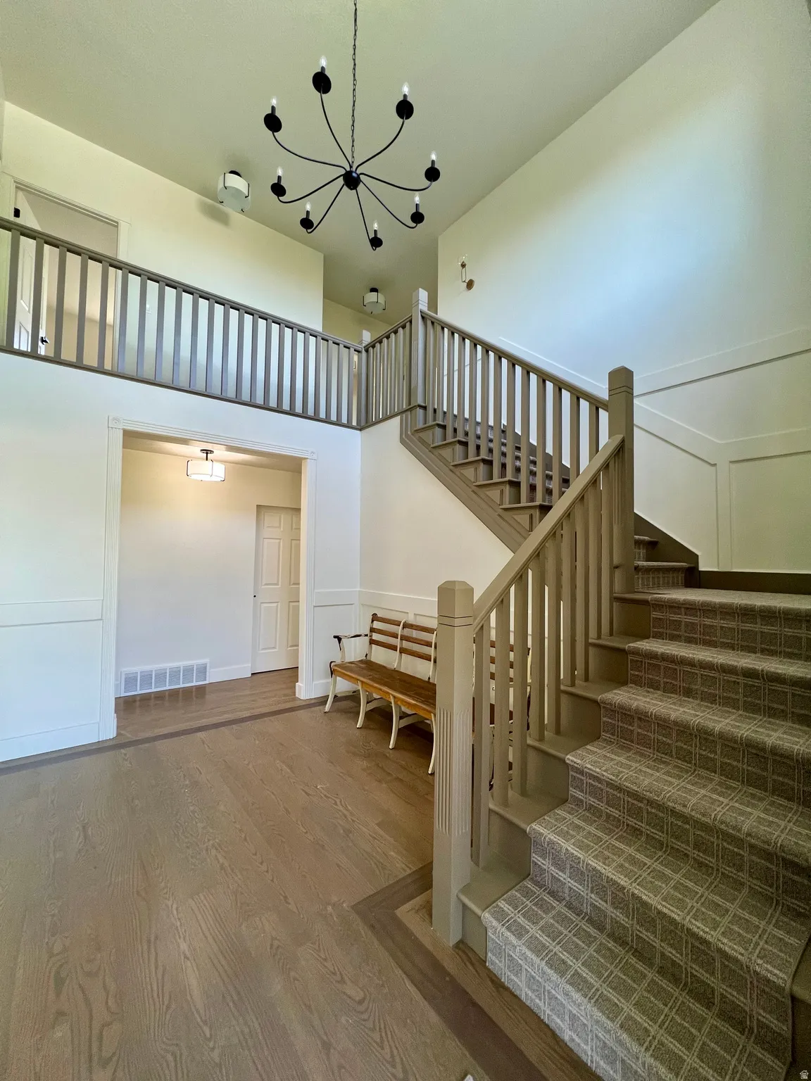Two-story foyer featuring an open staircase with carpeted treads and painted balusters, a coordinating upper-level railing, and a black multi-arm chandelier