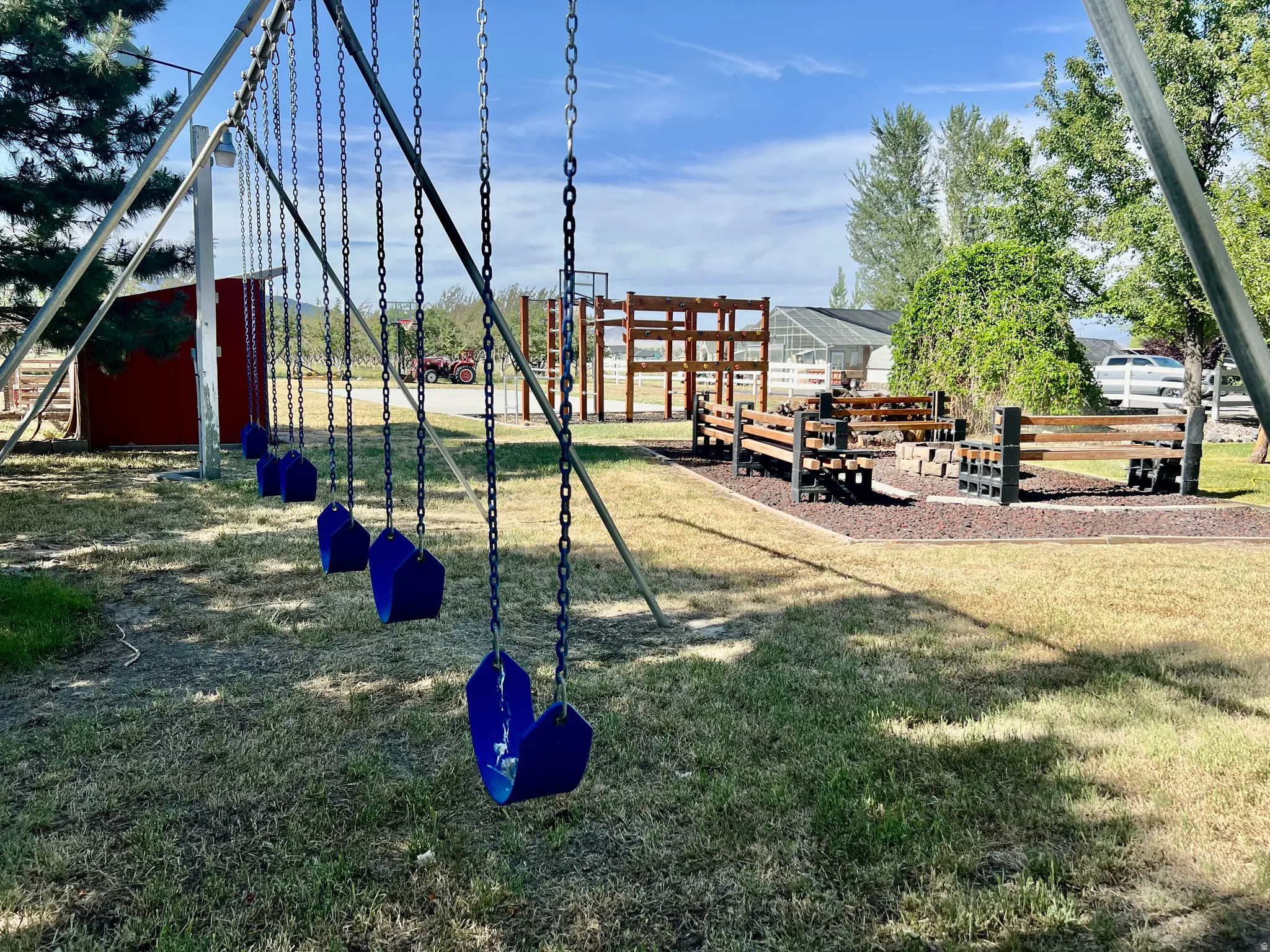 Expansive outdoor space featuring a multi-swing set, a fire pit area with built-in seating, a wooden play structure, and mature trees