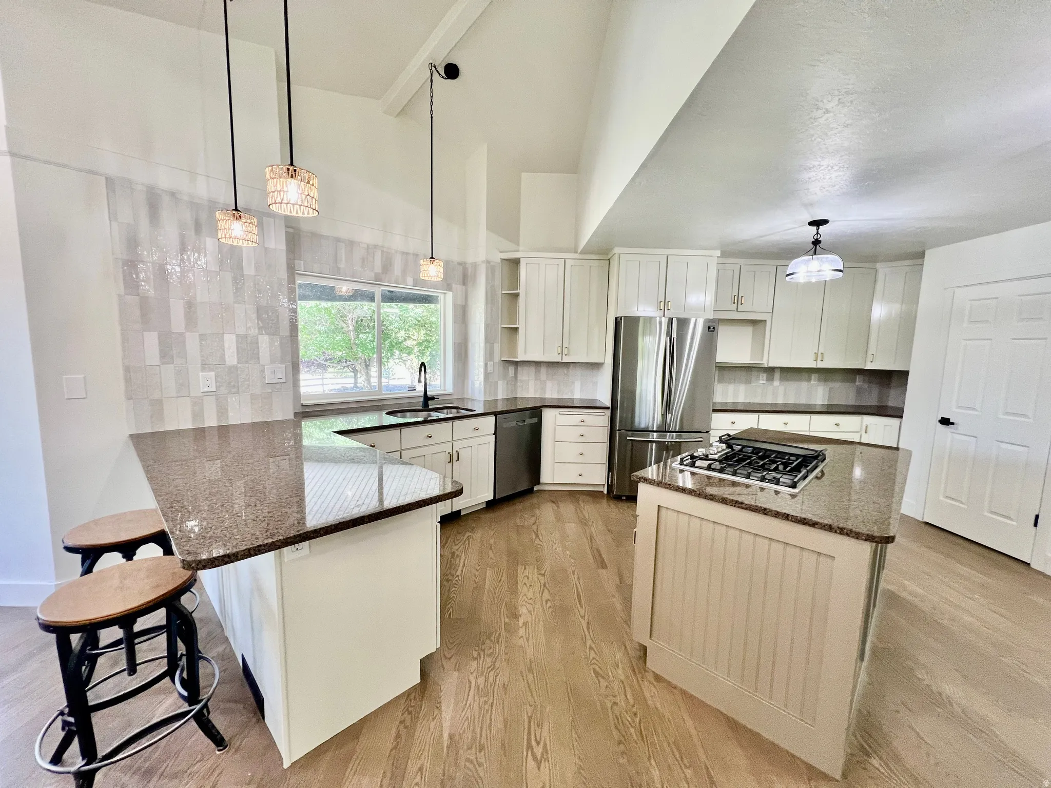 Kitchen featuring white shaker cabinetry, speckled countertops, a gas cooktop island, stainless steel appliances, and wood-finish flooring