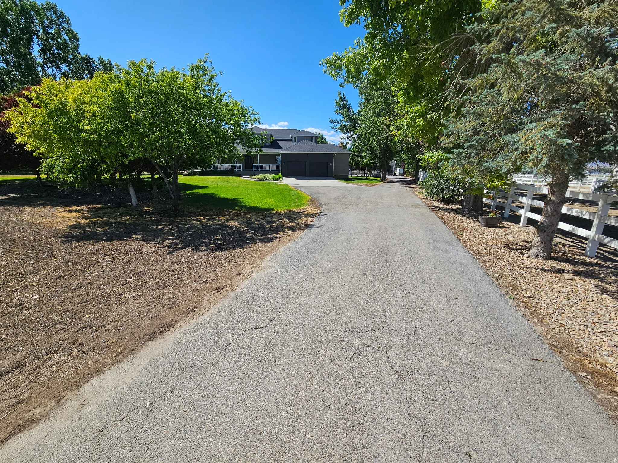 Paved driveway leading to a residence featuring a dark-toned facade, white porch columns, and a multi-car garage