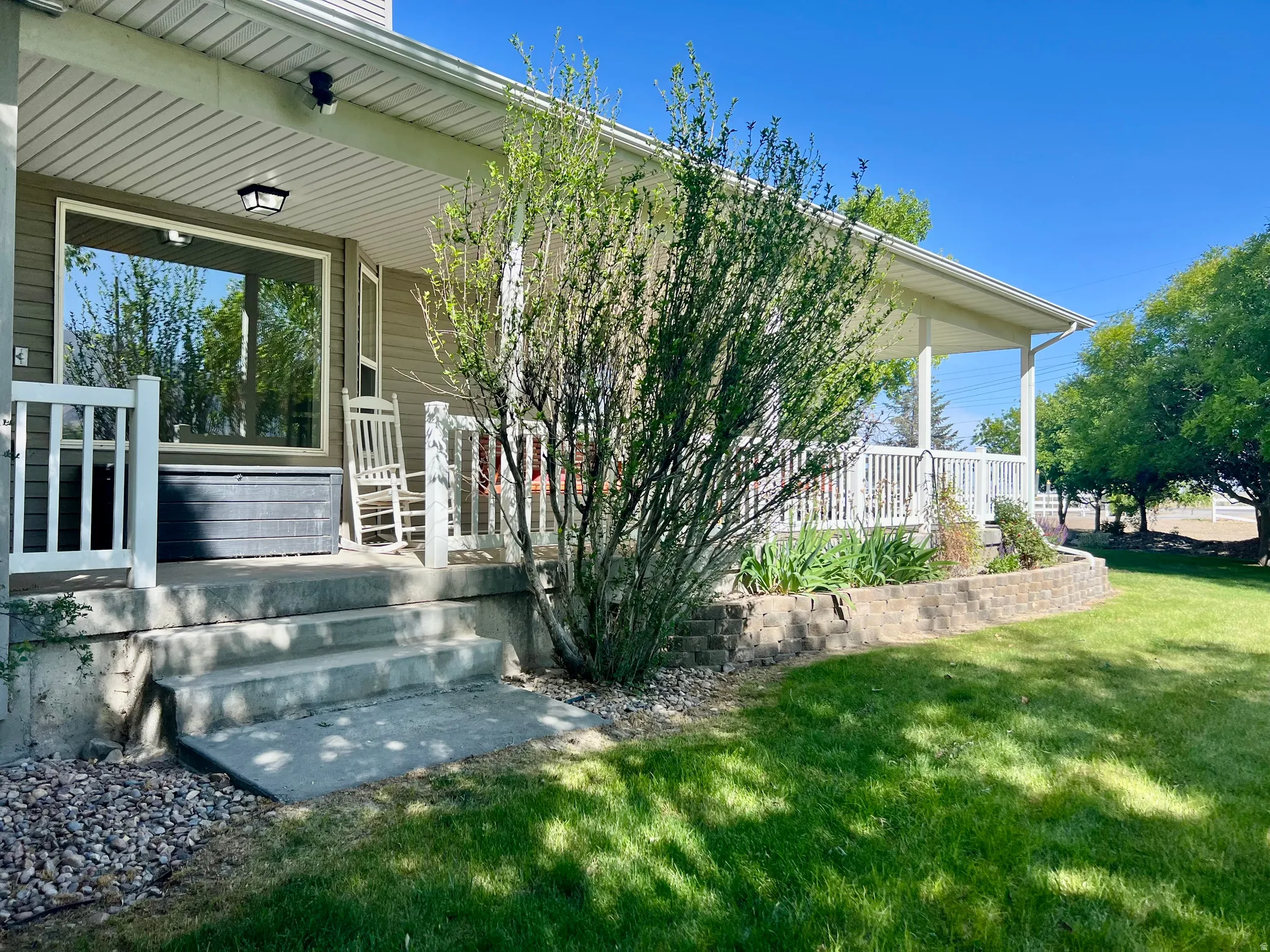 Covered porch with white railings, a large picture window, and exterior lighting fixture