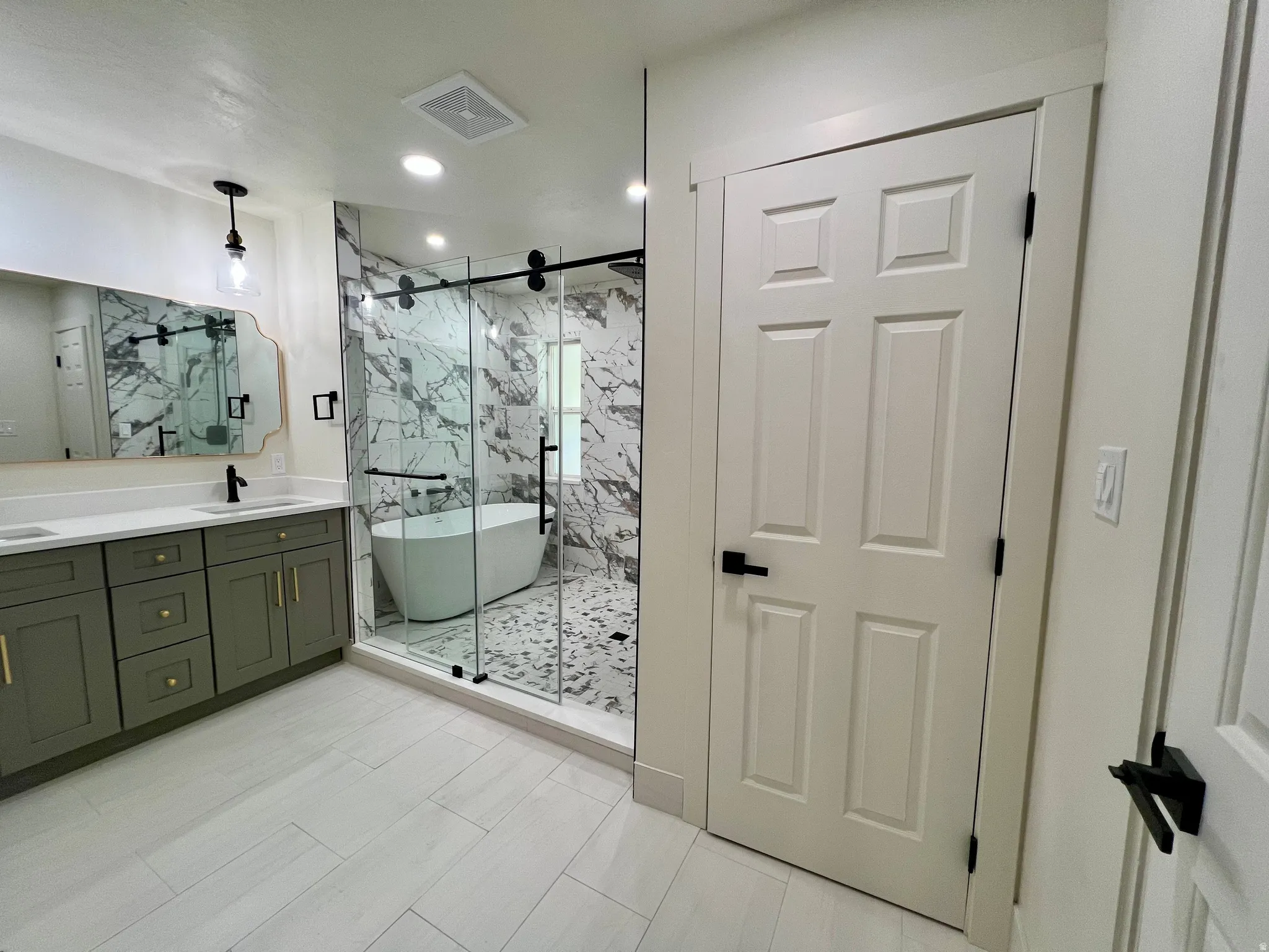 Spacious bathroom featuring a freestanding tub within a glass-enclosed shower, dual vanity with green cabinetry, white countertops, and light tile flooring