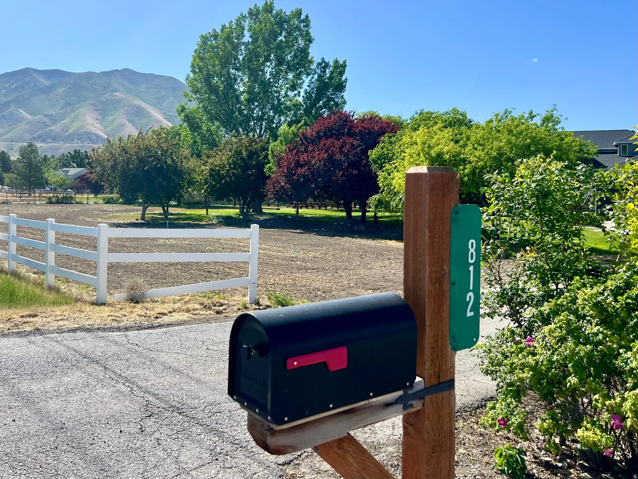 Property entrance featuring a black mailbox on a wooden post with an address marker, bordered by a white fence