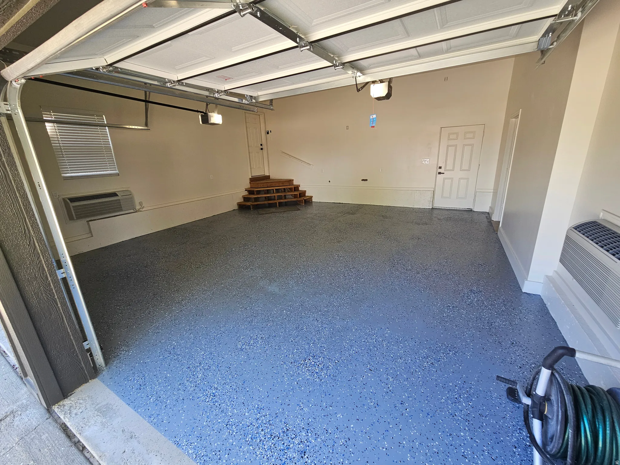 Spacious garage featuring a durable epoxy floor finish, dedicated door access, interior window with blinds, and built-in wall unit