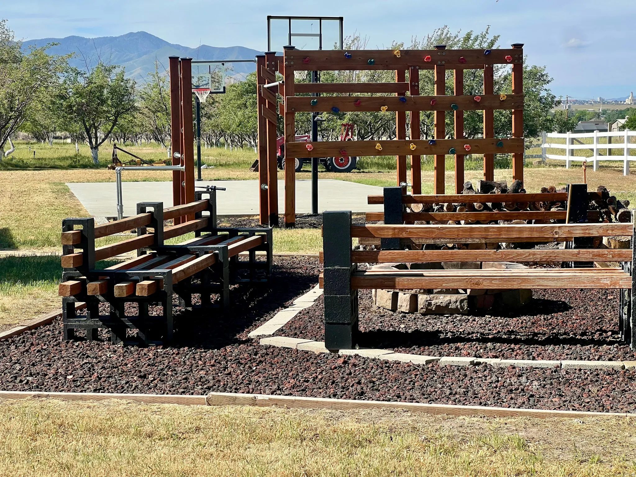 Outdoor activity area featuring a basketball hoop, a wooden climbing structure with handholds, and a dedicated fire pit area