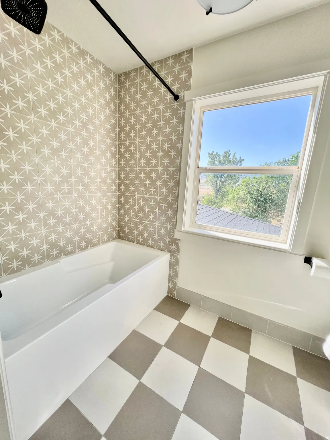 Full bathtub with patterned wall tile, checkered floor tile, and a single window