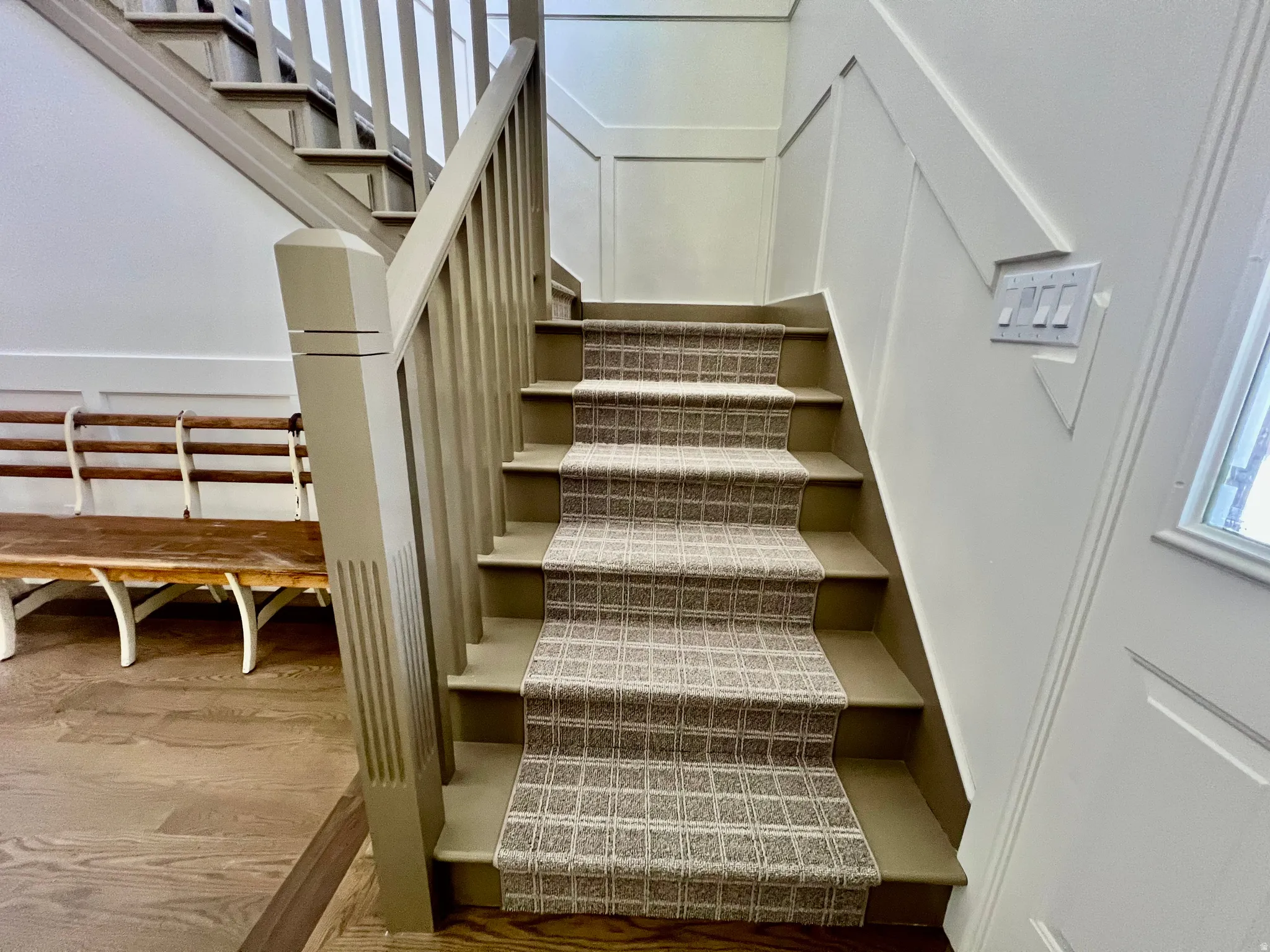 Staircase featuring a patterned carpet runner, painted balusters and newel post, and wainscoting paneling
