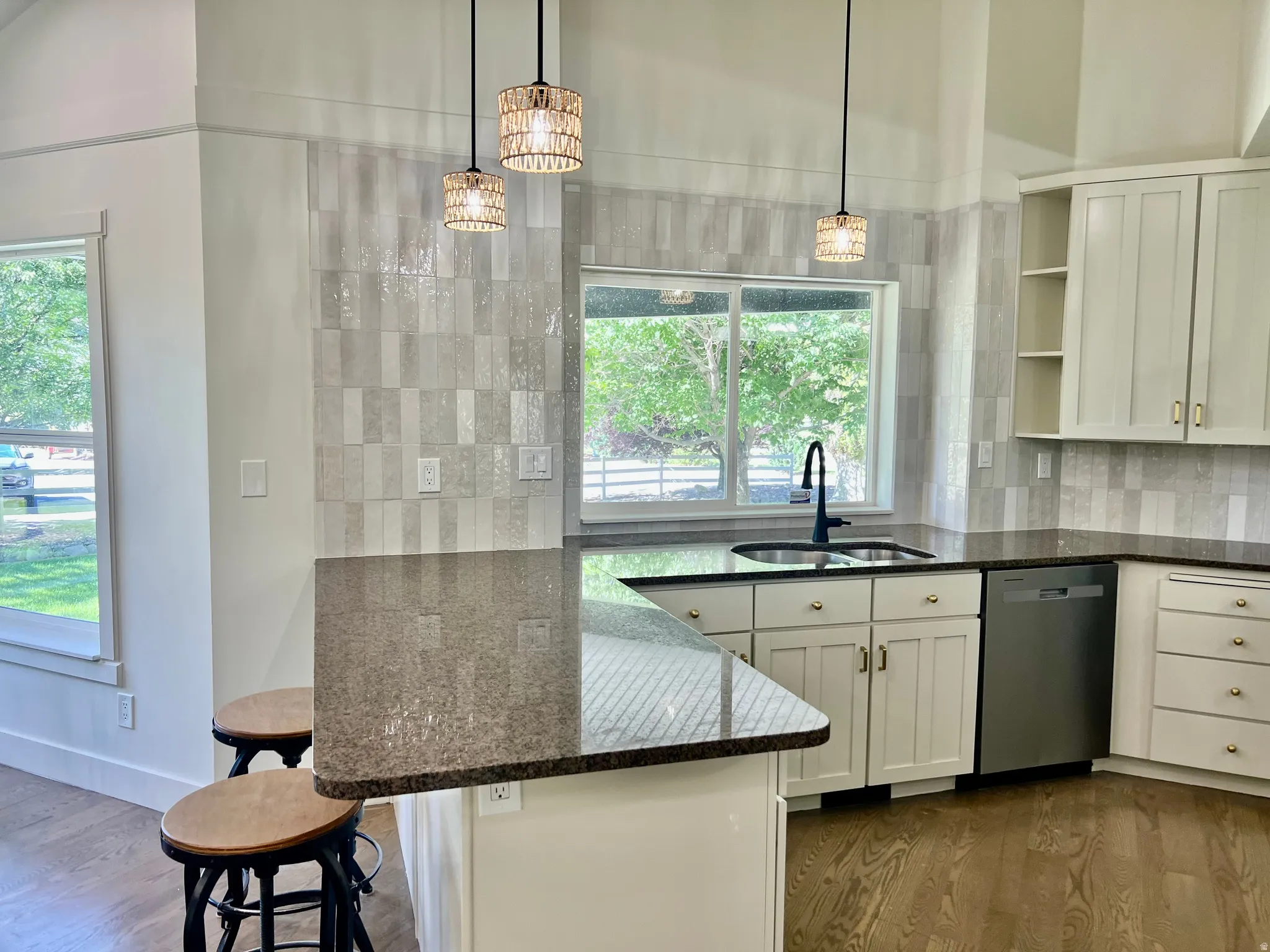 Kitchen featuring a breakfast bar with stone countertop, stainless steel sink with matte black faucet, full-height tile backsplash, white cabinetry, and wood-finish flooring
