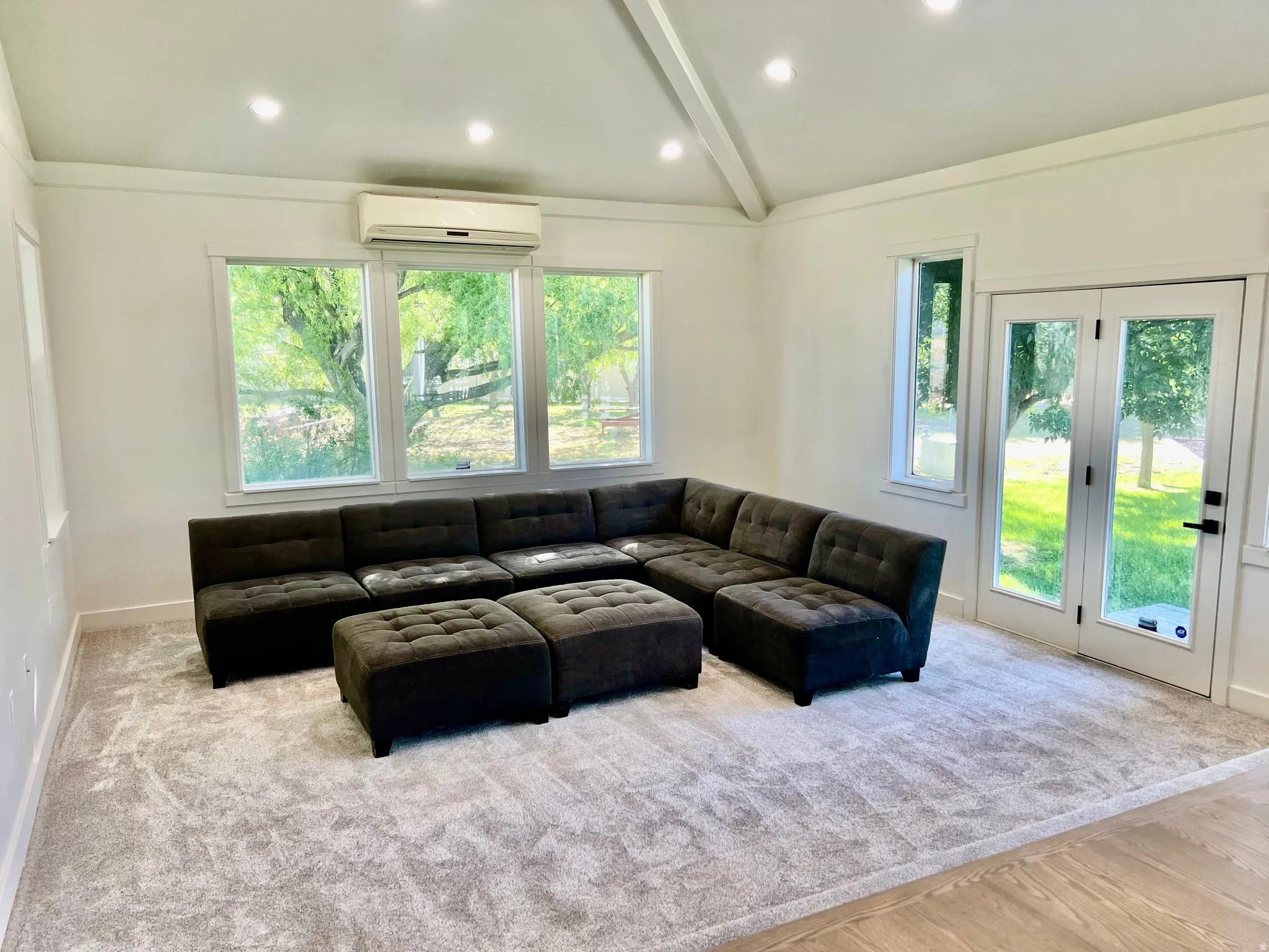 Spacious room featuring vaulted ceilings, recessed lighting, expansive windows, French doors, and new carpet flooring