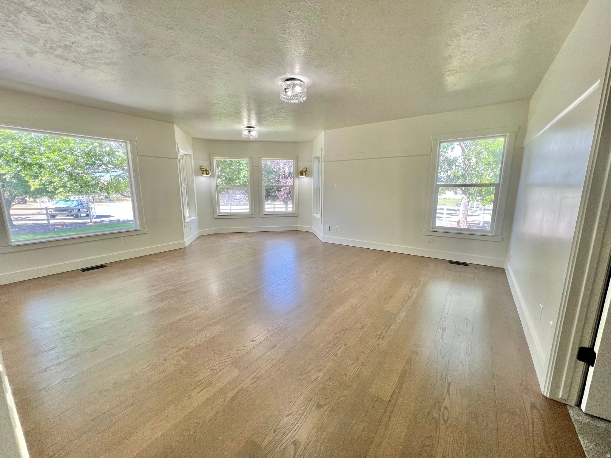 Expansive room featuring light wood-finish flooring, multiple windows providing natural light, white trim, recessed lighting, and wall sconces