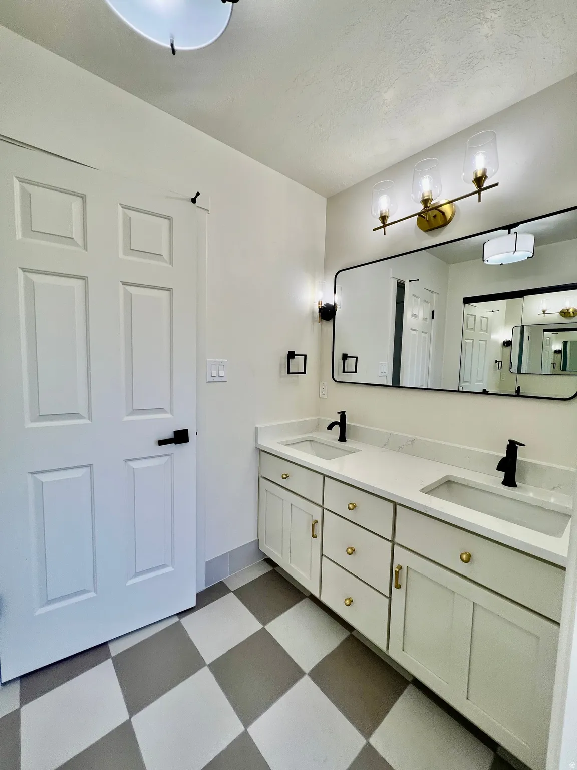 Bathroom featuring a double vanity with white cabinetry, gold-toned hardware, and white countertops