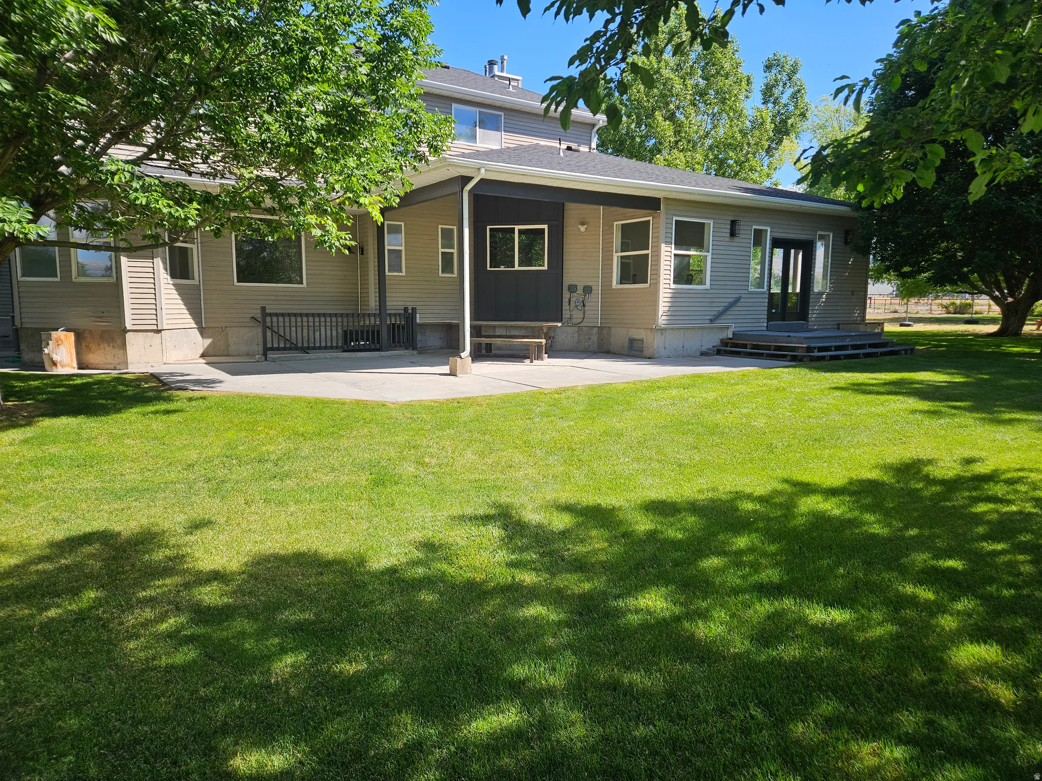 Expansive rear yard featuring a large concrete patio, mature trees, and a dual-pane glass entry door with sidelights