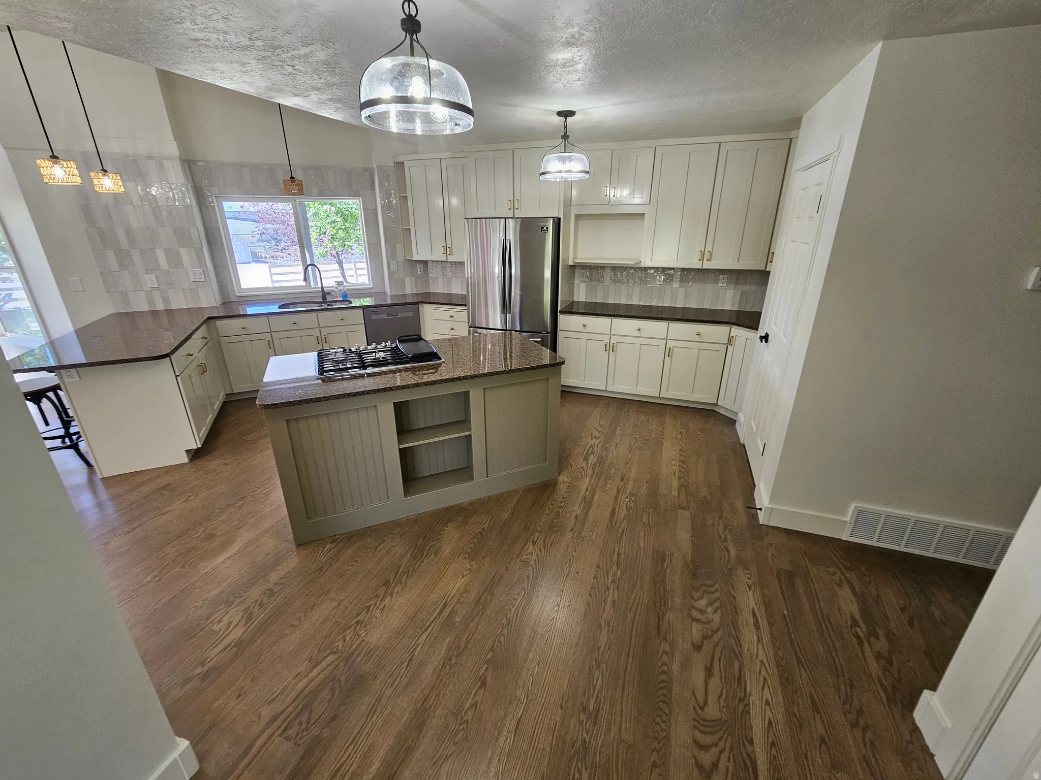 Spacious kitchen featuring wood-finish flooring, an island with built-in cooktop, light-toned cabinetry, and stainless steel appliances