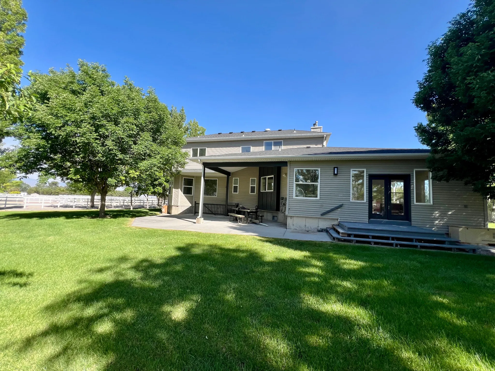 Expansive rear yard featuring a manicured lawn, mature shade trees, a covered patio, and a multi-level deck with direct access to the interior
