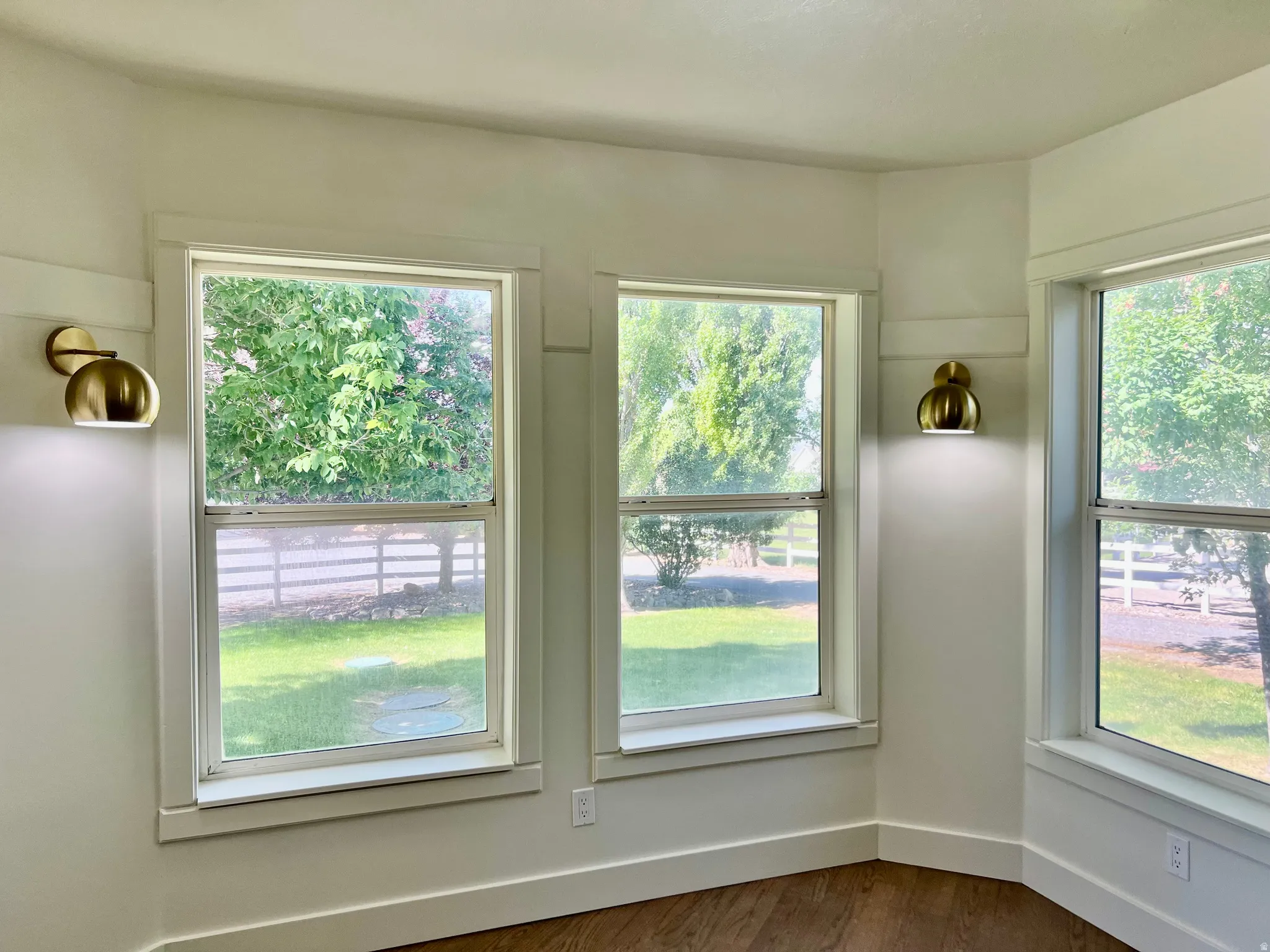 Bright interior space featuring multiple double-hung windows, contemporary brass wall sconces, wood-finish flooring, white baseboards, and white wall trim