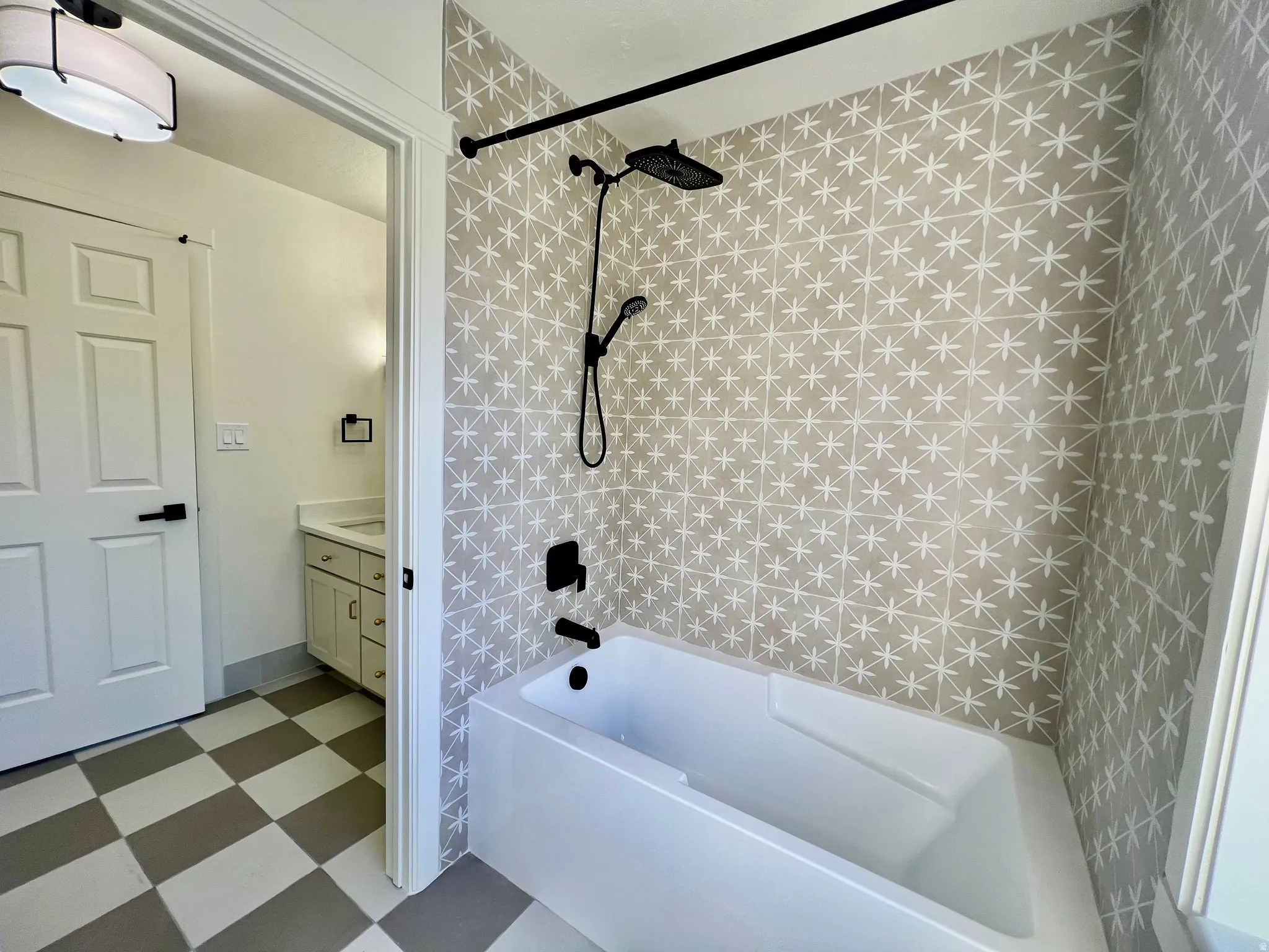 Bathroom featuring a white soaking tub with matte black fixtures, an accent wall with patterned tile, and checkered flooring