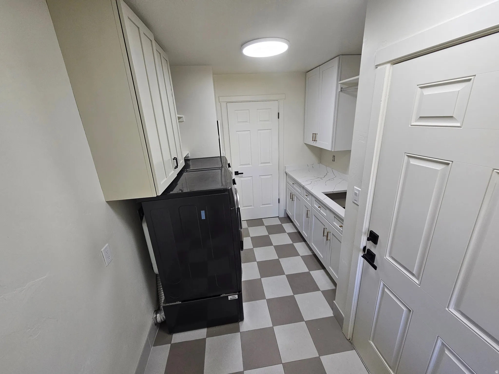 Utility room featuring checkerboard flooring, white cabinetry, a built-in sink, and white paneled doors