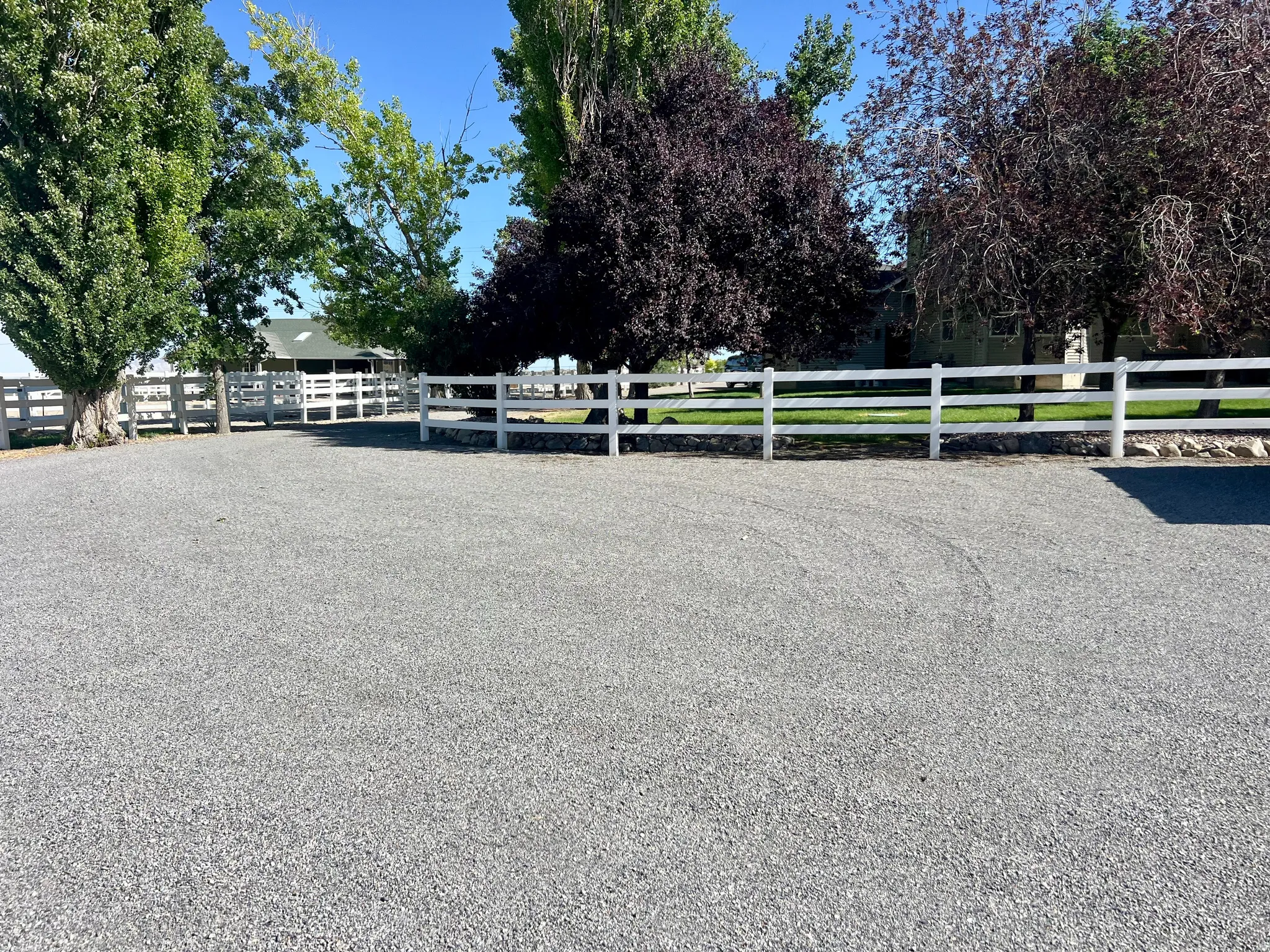 Gravel drive with white three-rail fencing, bordered by mature trees and verdant lawns