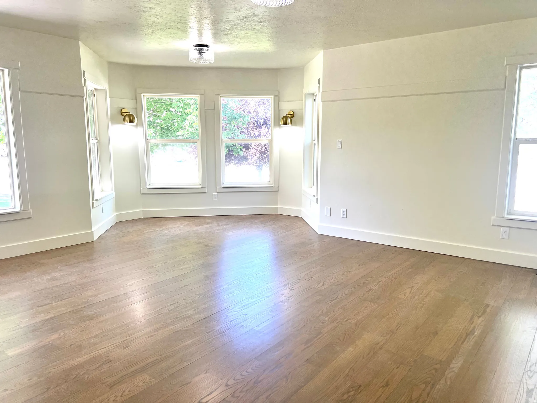Spacious room featuring wood-finish flooring, white trim, and multiple windows