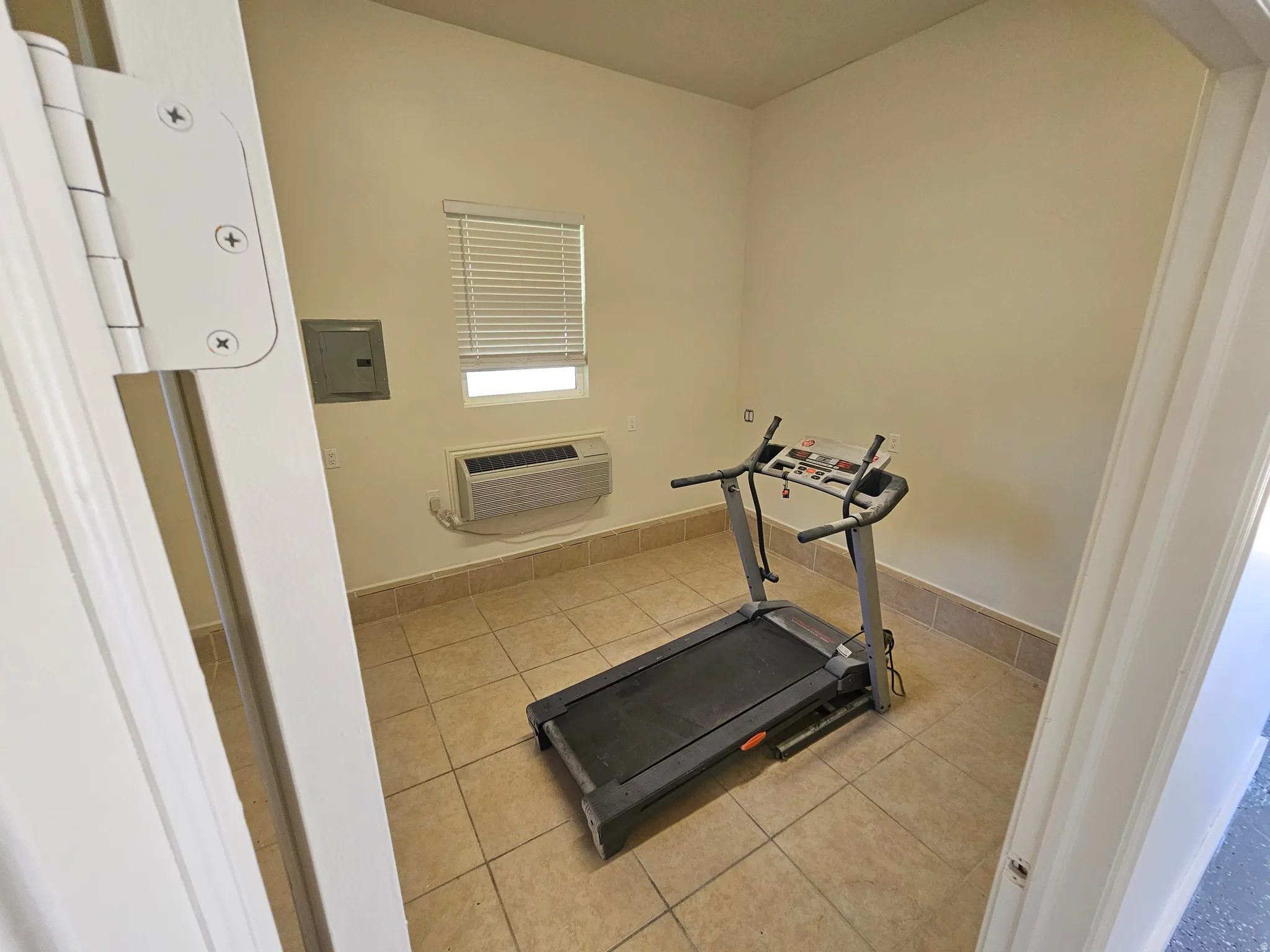 Versatile room featuring tile flooring, neutral wall tones, a window with blinds, and a wall-mounted air conditioning unit