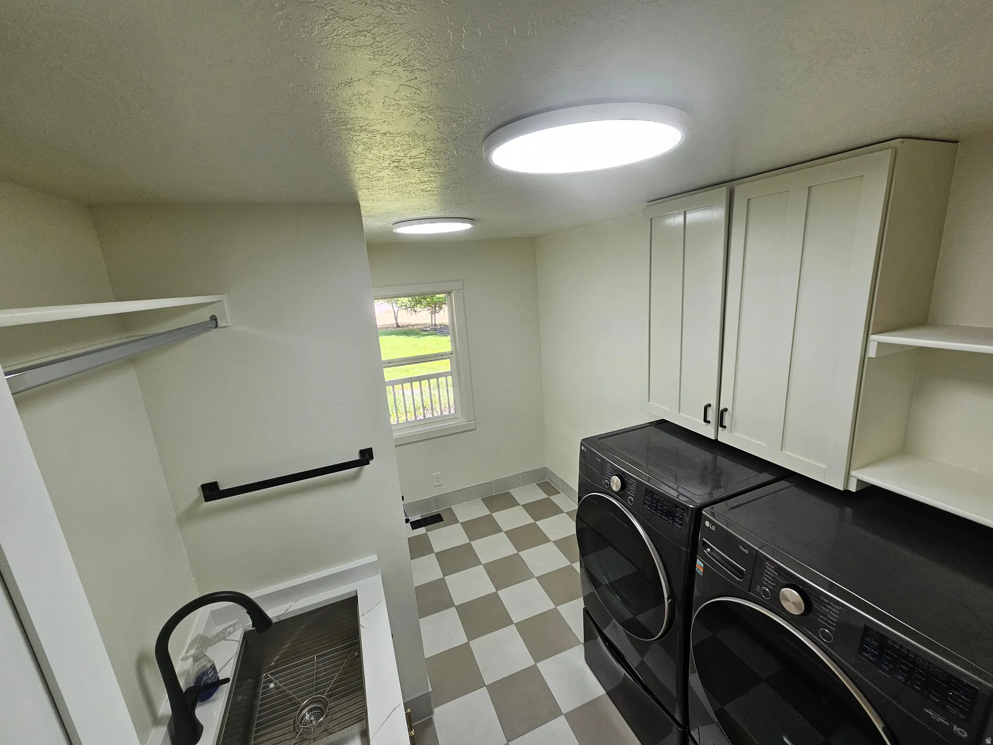 Functional utility space featuring checkerboard tile flooring, built-in cabinetry, an integrated sink with a matte black faucet, and overhead shelving