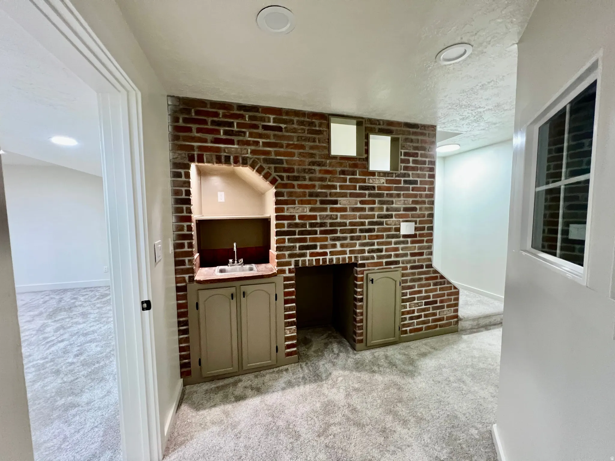 Exposed brick wall featuring a built-in wet bar with a sink and storage cabinetry, recessed lighting, and soft gray carpeting