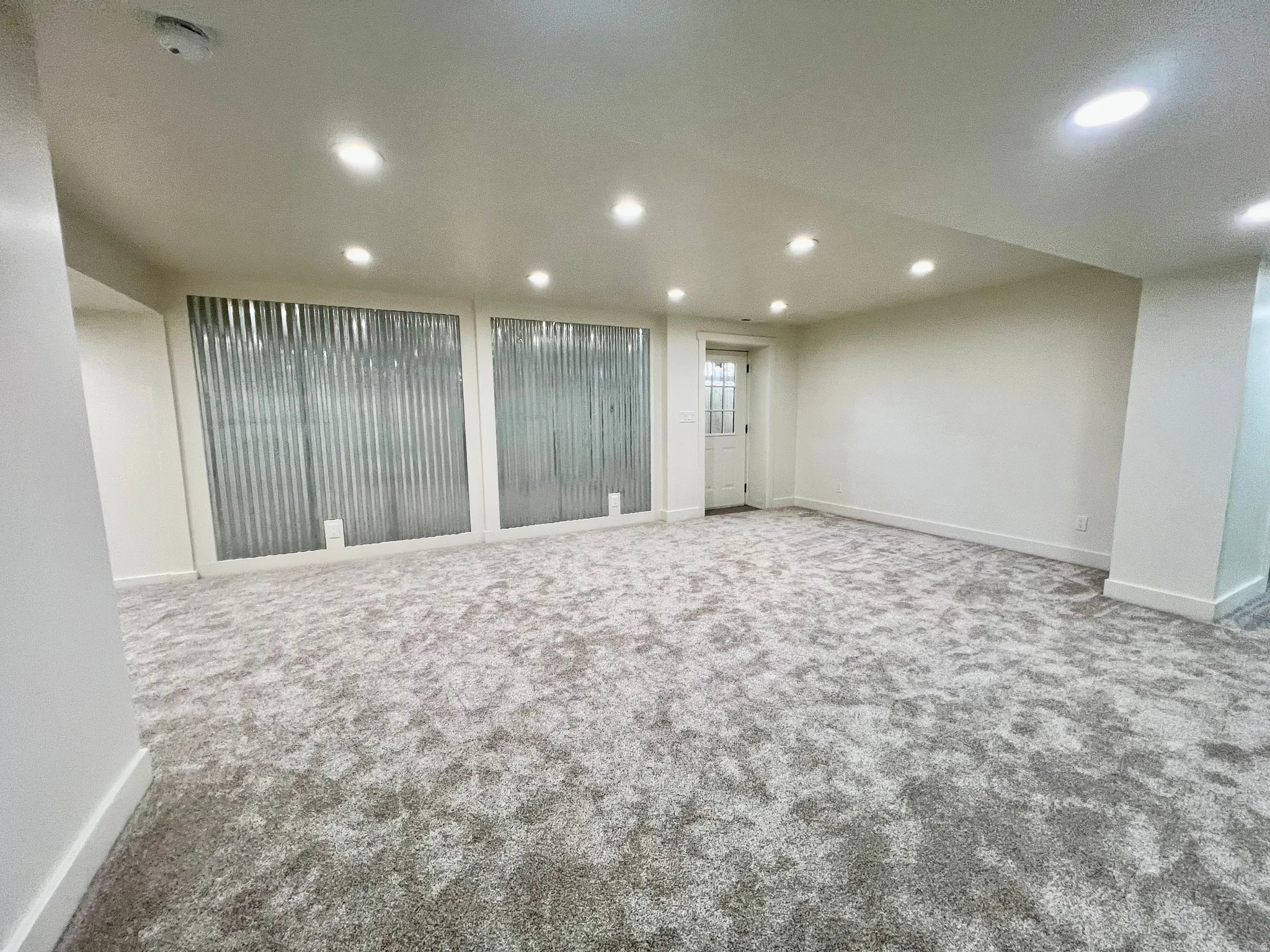 Spacious room featuring new patterned carpeting, recessed ceiling lighting, and crisp white baseboards