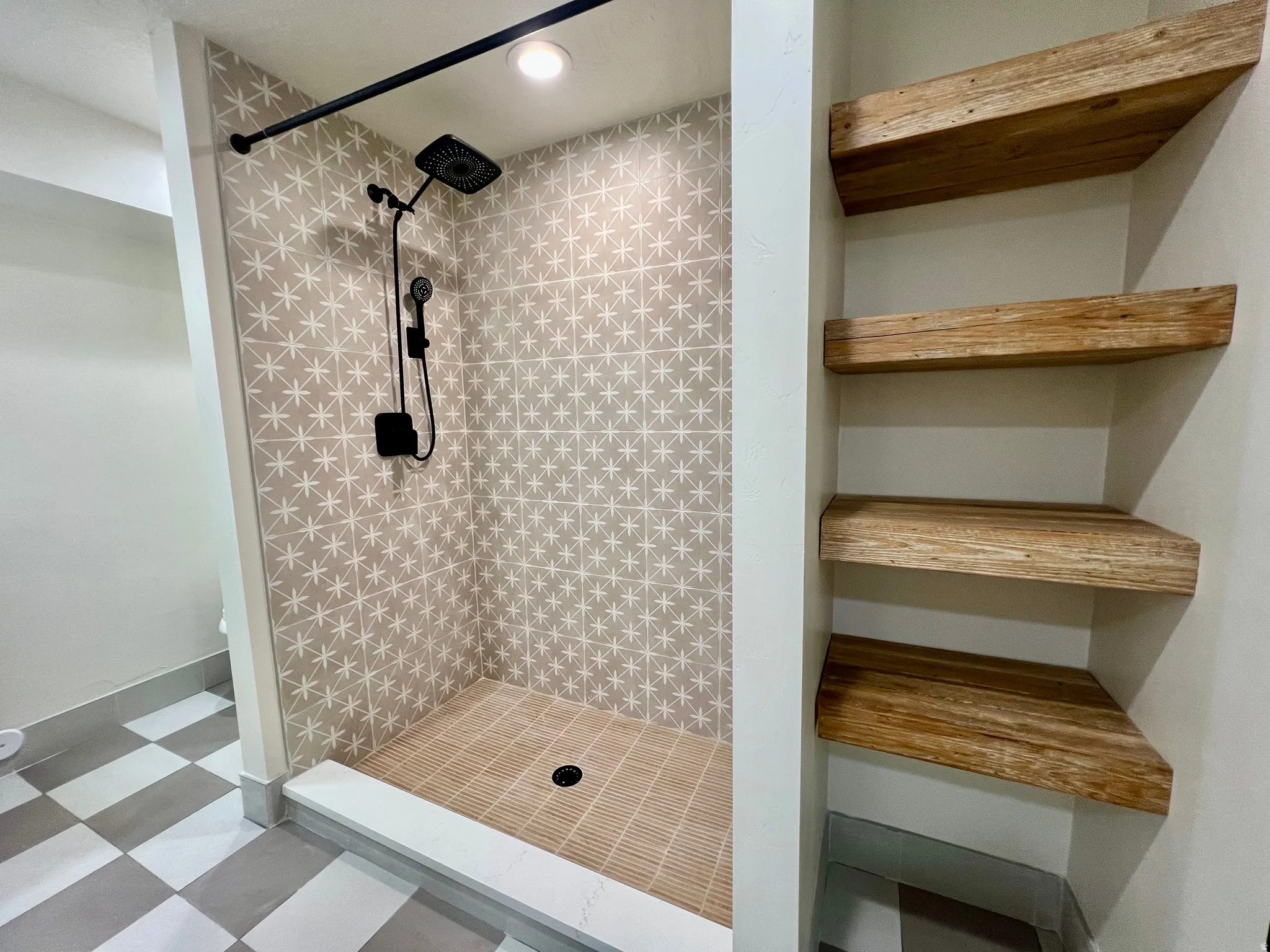 Walk-in shower featuring patterned wall tiles, a rainfall showerhead, and a handheld sprayer with matte black finishes