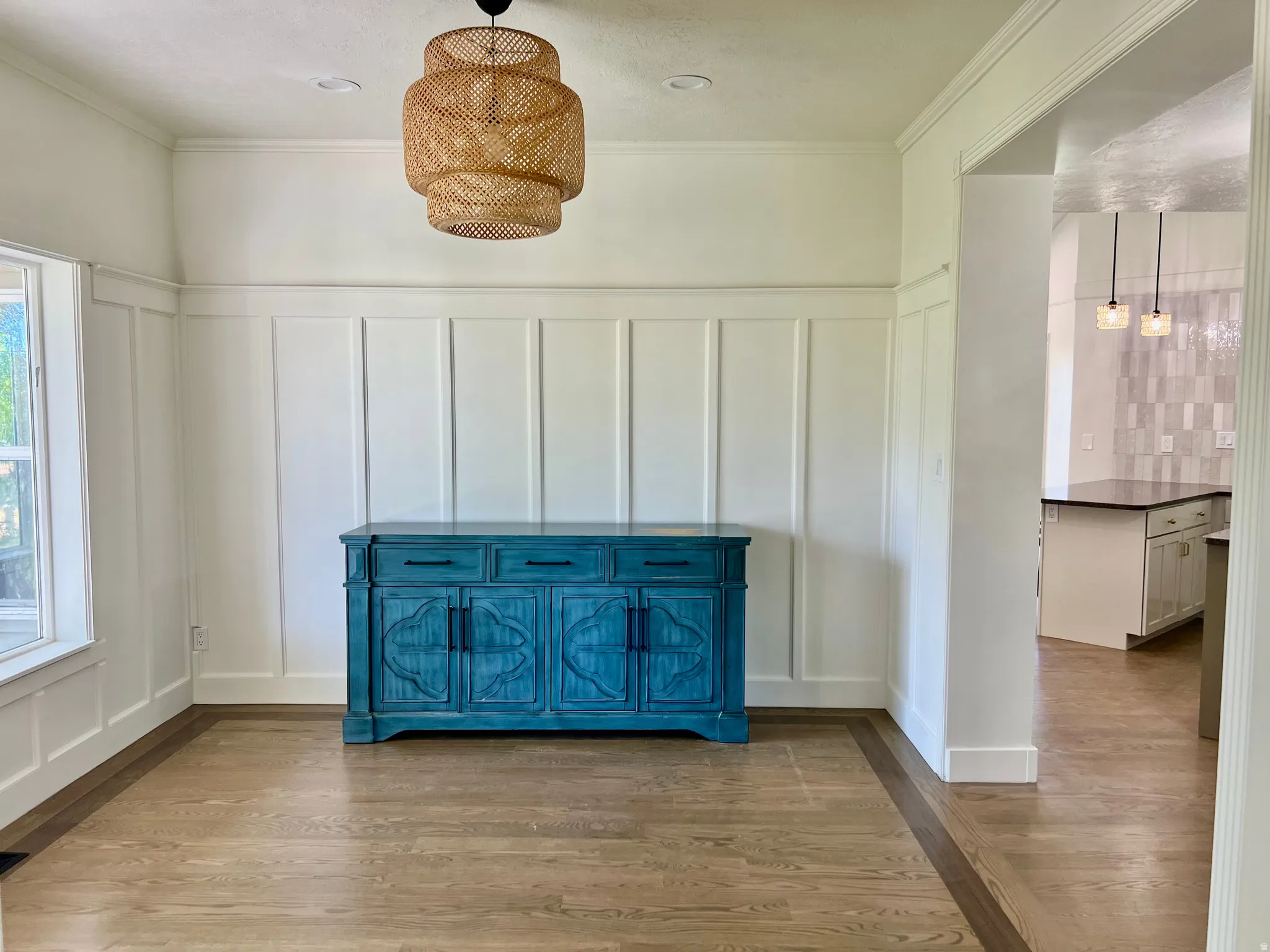 Board and batten wainscoting in a bright room with light wood-finish flooring featuring a dark wood-finish border