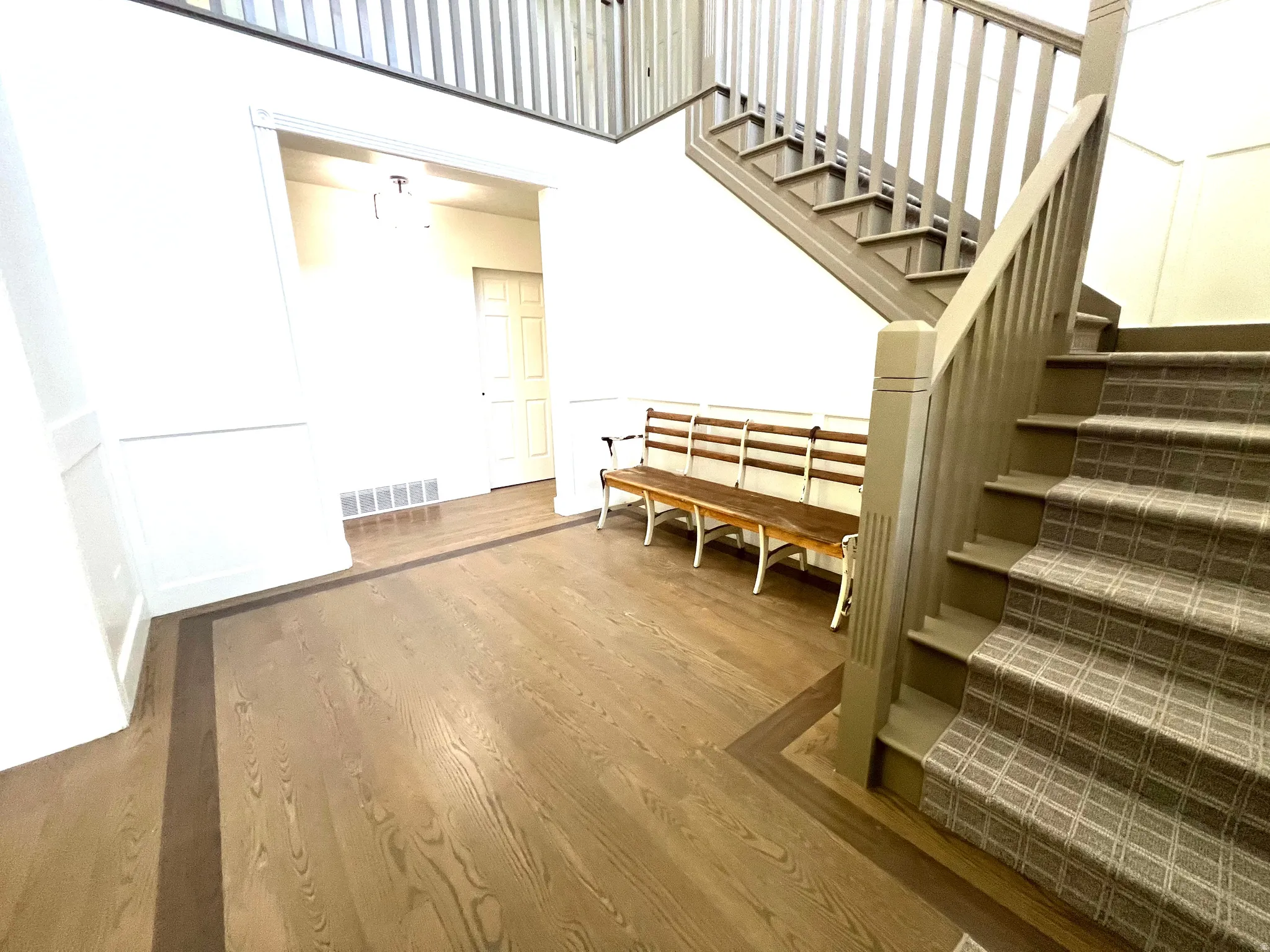 Entryway featuring wood-finish flooring with a dark border inlay, wainscoting details, and a staircase with patterned carpeting and painted wood railings