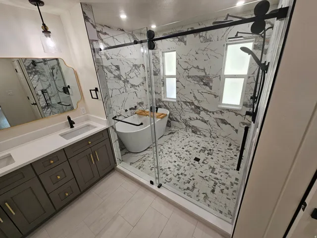 Bathroom featuring a dual vanity with a light-toned countertop, a frameless glass shower enclosure, a freestanding soaking tub, and a multi-function shower system