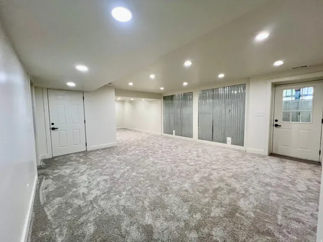 Spacious finished room featuring recessed lighting, light-toned textured carpet, white panel doors, and corrugated metal wall accents