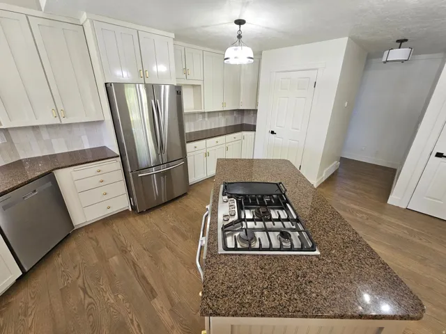 Kitchen featuring an island with an integrated gas cooktop, white cabinetry with gold-tone hardware, stainless steel appliances, speckled countertops, and wood-finish flooring