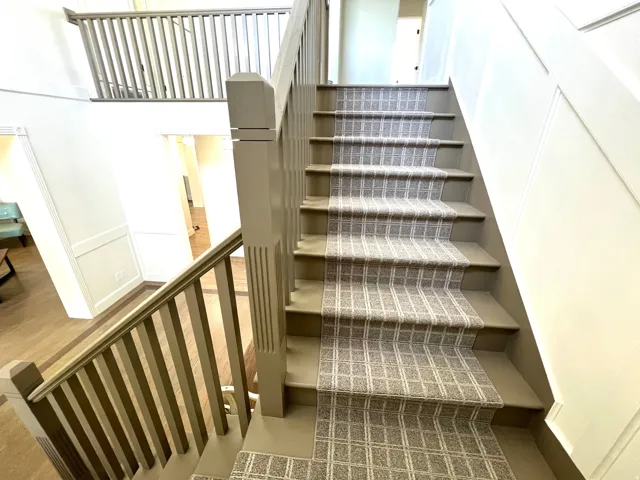 Staircase with patterned runner, painted balusters, and a paneled wall