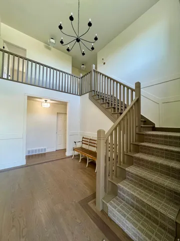 Two-story foyer featuring an open staircase with carpeted treads and painted balusters, a coordinating upper-level railing, and a black multi-arm chandelier