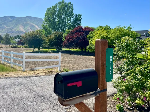 Property entrance featuring a black mailbox on a wooden post with an address marker, bordered by a white fence