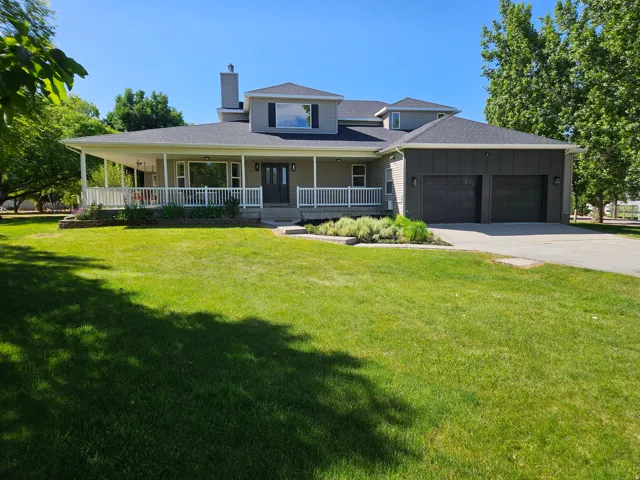 Contemporary-style residence featuring a broad covered front porch with white railings, a two-car garage with dark paneled doors, and a stone-clad chimney