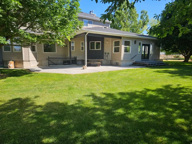 Expansive rear yard featuring a large concrete patio, mature trees, and a dual-pane glass entry door with sidelights