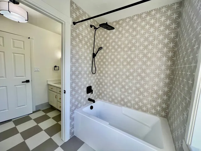 Bathroom featuring a white soaking tub with matte black fixtures, an accent wall with patterned tile, and checkered flooring