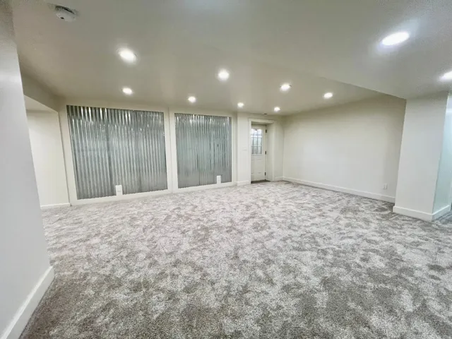 Spacious room featuring new patterned carpeting, recessed ceiling lighting, and crisp white baseboards