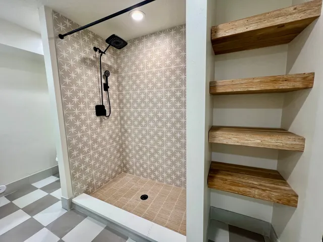 Walk-in shower featuring patterned wall tiles, a rainfall showerhead, and a handheld sprayer with matte black finishes